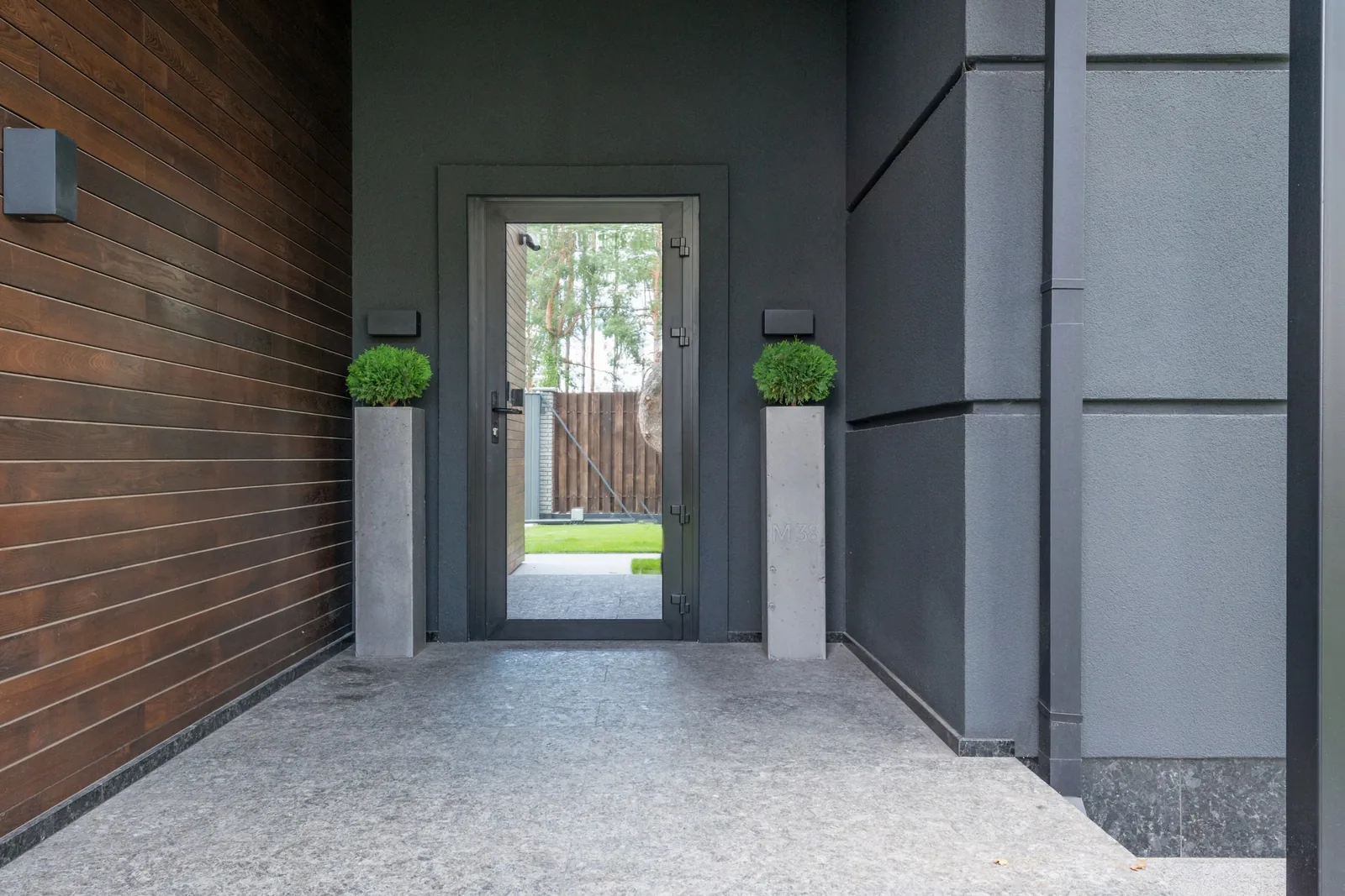 Entrée vitrée noire d’une façade contemporaine encadrée par deux grands pots plantés